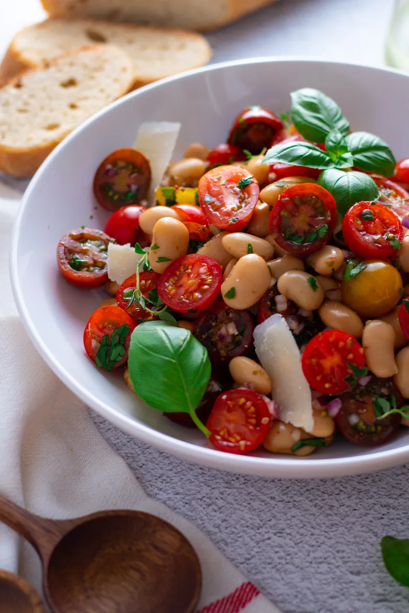 Cherry Tomato and White Bean Salad in a bowl with wooden salad servers and a baguette.
