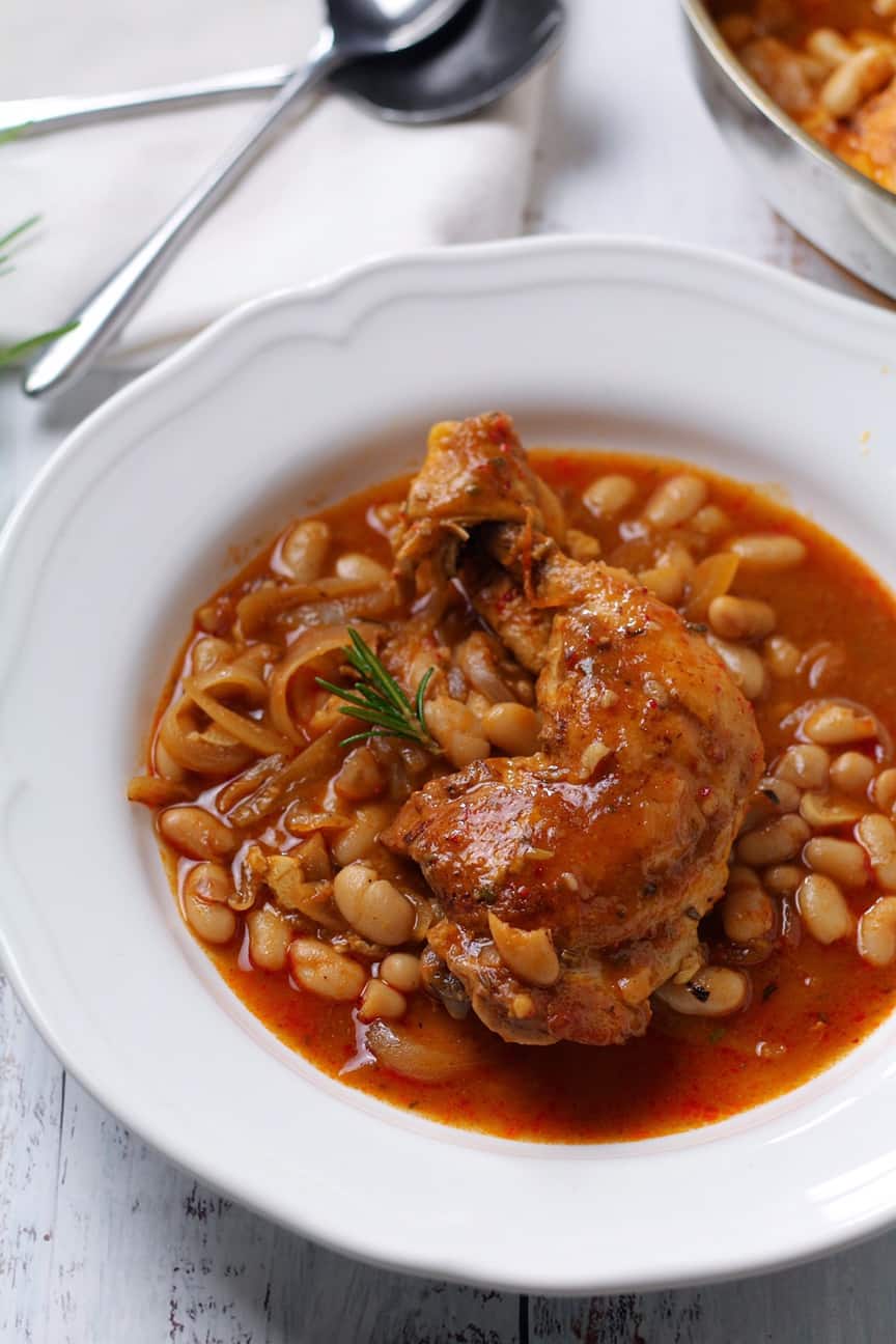 Chicken and white bean stew in a white bowl, garnished with rosemary.