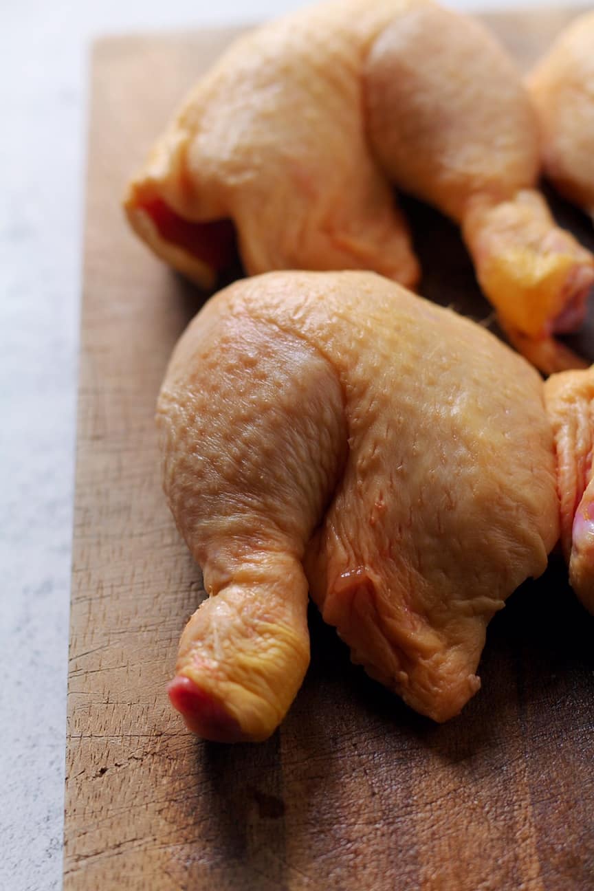 Raw chicken legs on a wooden cutting board, ready for braising.