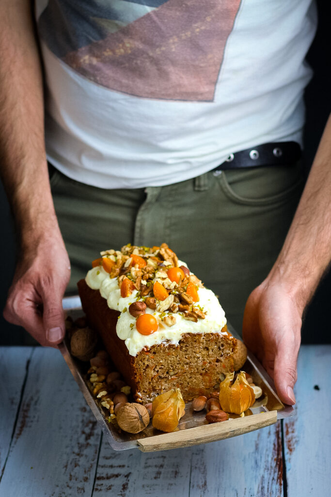 Jay Wadams holding a baked a decorated carrot cake loaf with cream cheese frosting.