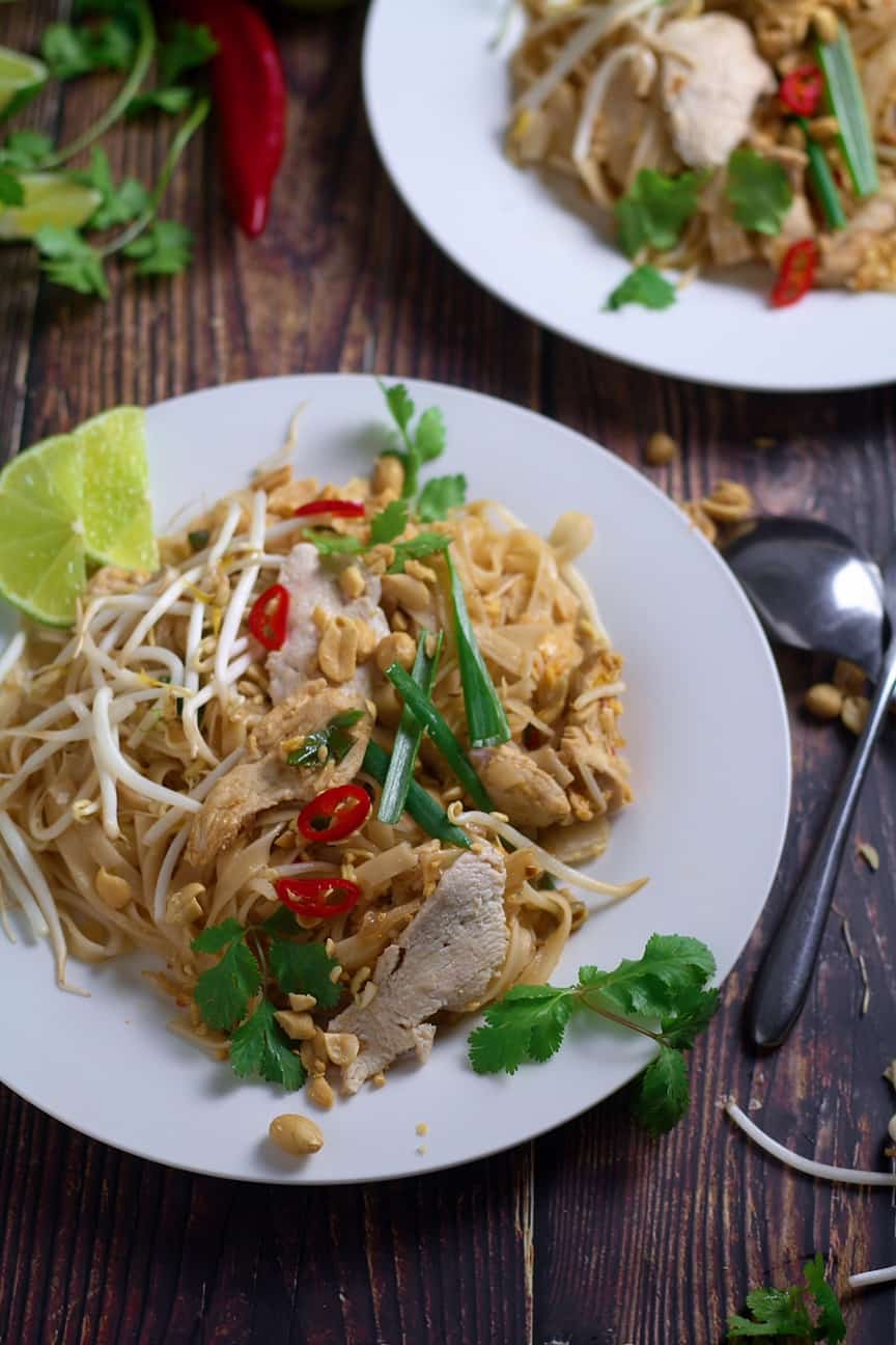 Plate of delicious Pad Thai with chicken, bean sprouts, peanuts, cilantro, lime wedge, and chili pepper garnish.