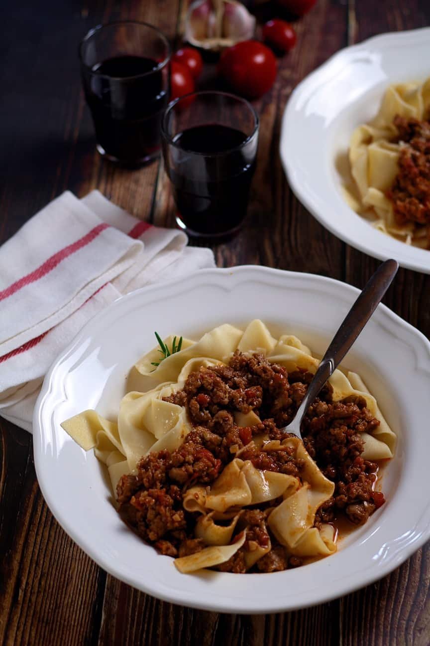 Rustic Pork and Fennel Ragu on a wooden table with two glasses of Italian red wine.