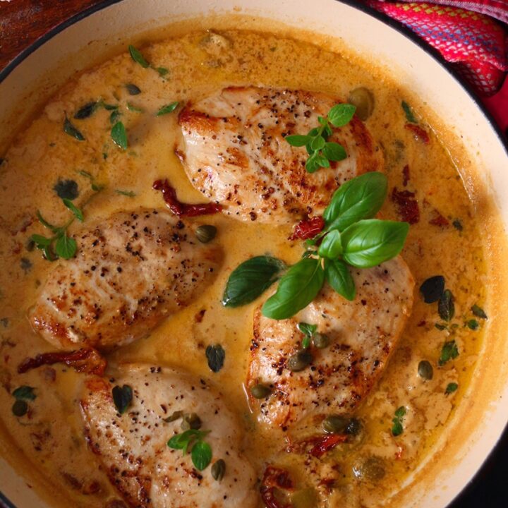 Chicken breasts in a creamy sun dried tomato and basil sauce in a red pan