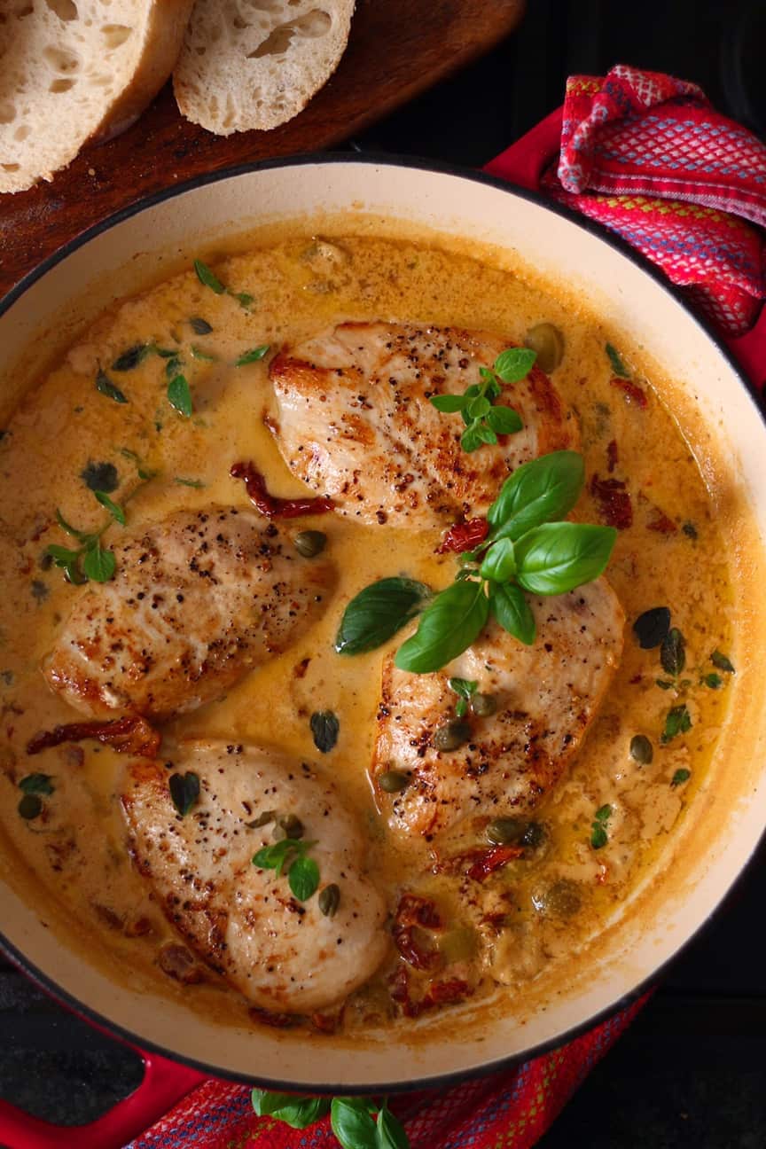Chicken breasts in a creamy sun dried tomato and basil sauce in a red pan