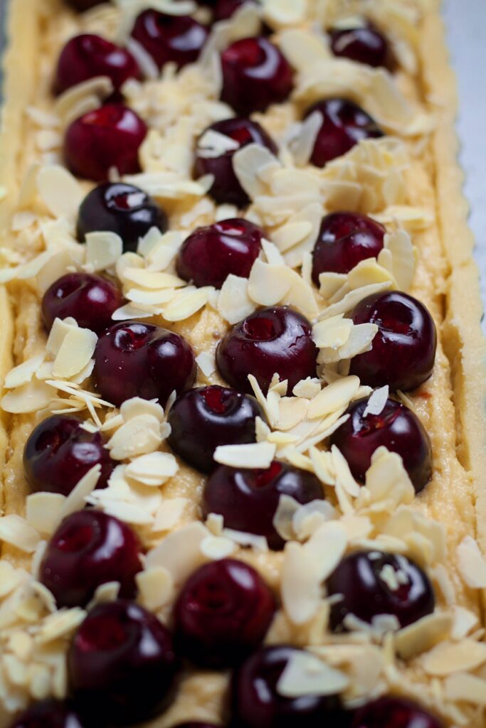 Long fluted tart pan filled with frangipane filling and cherries. Topped with flaked almonds.