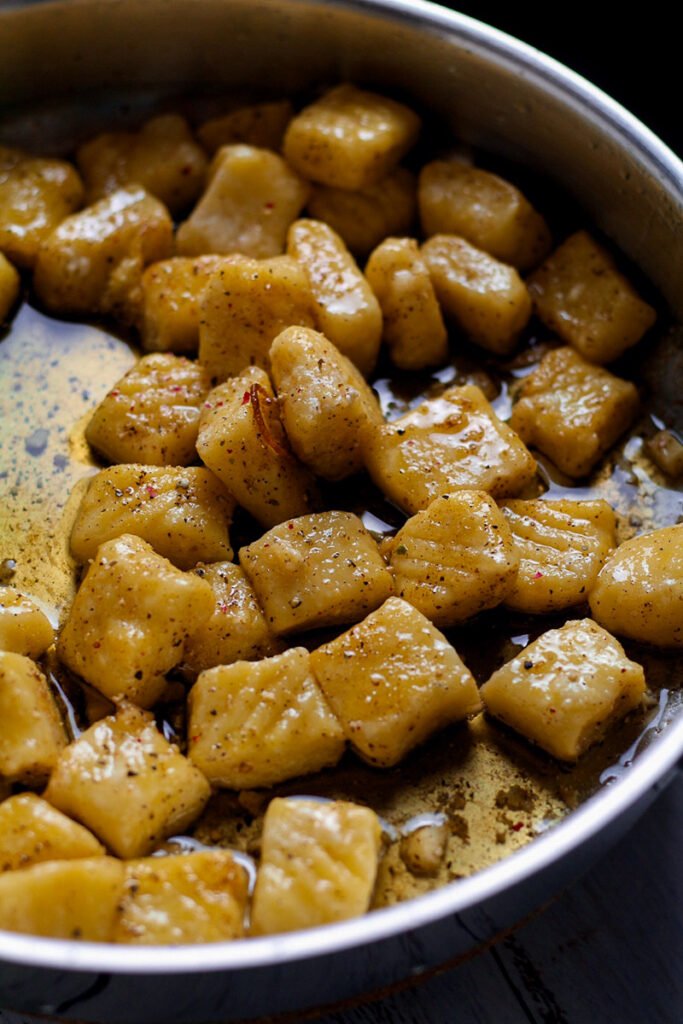 Ricotta gnocchi frying in a skillet of browned butter.