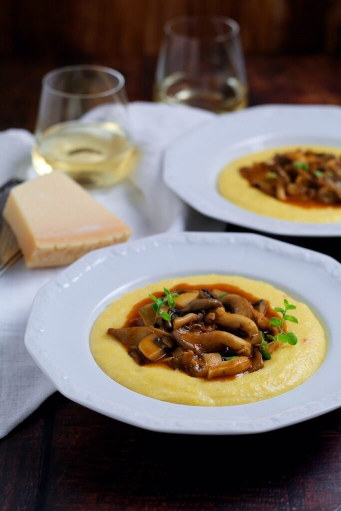 Mushrooms with Creamy Polenta in a bowl with Parmesan cheese and glasses of white wine.
