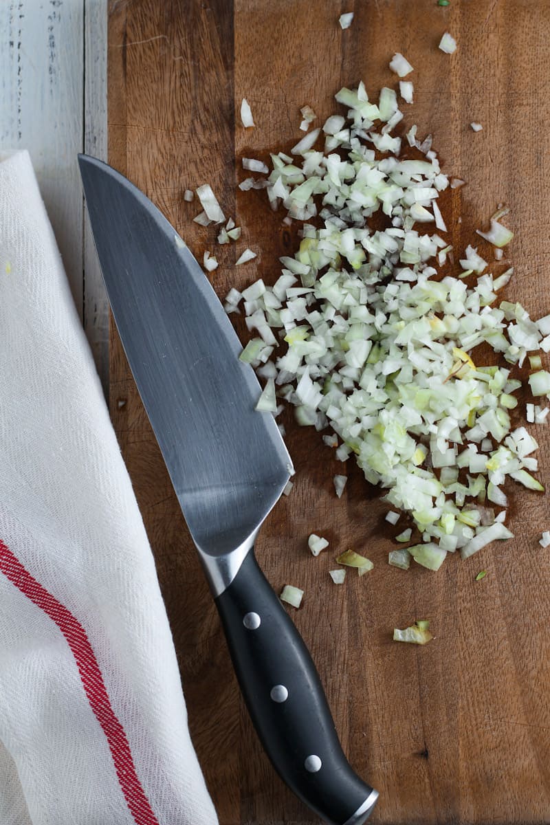 Diced onion on a wooden cutting board with a chef's knife.