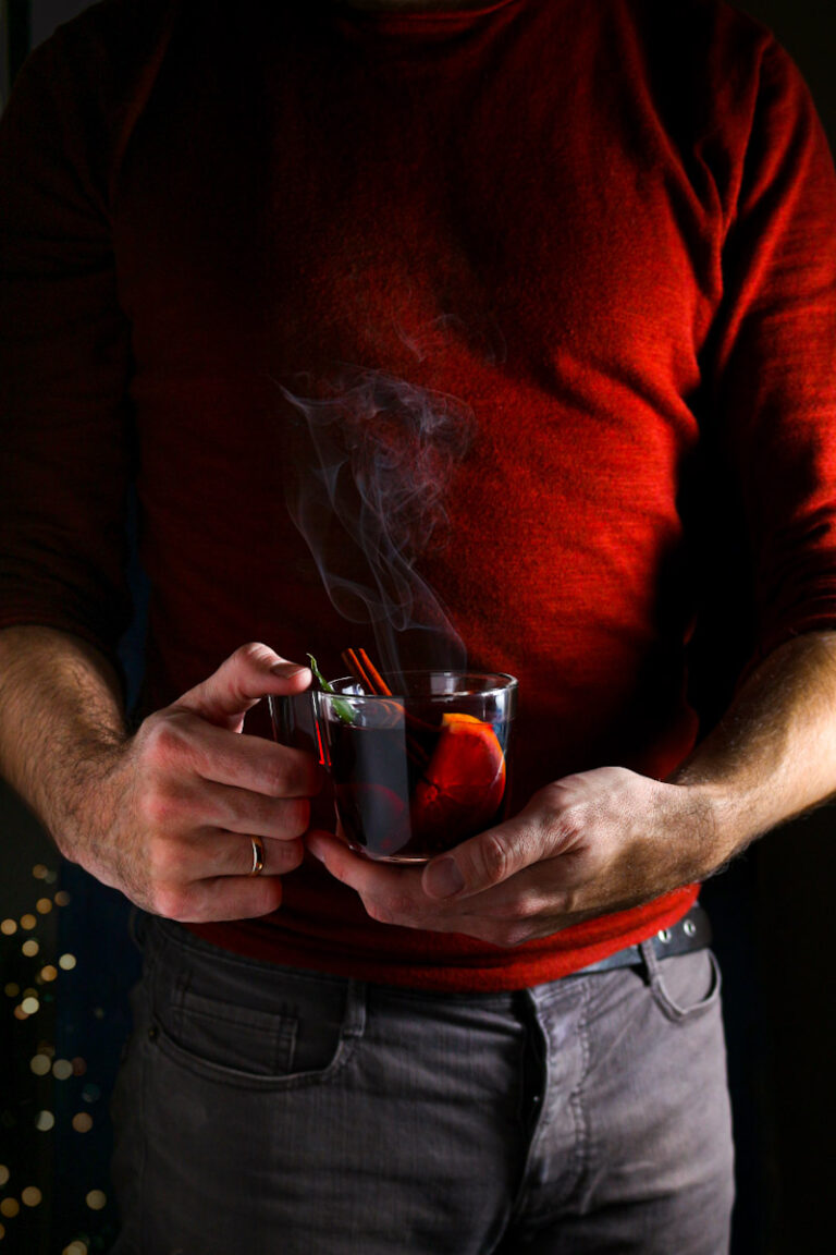 German Mulled wine recipe title card showing a mug of Glühwein and a man holding a mug of mulled wine.