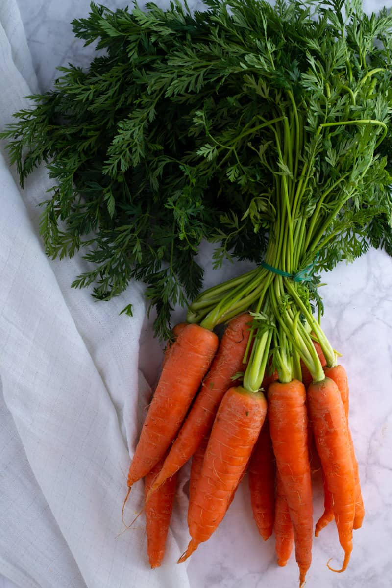 Fresh carrots with carrot greens attached on a white background.