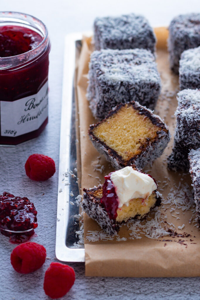 Lamington cakes on a tray with raspberry jam and whipped cream