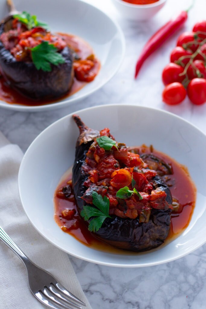 A picture of Imam Bayildi, roast Turkish eggplants stuffed with tomatoes and onions in a white bowl 