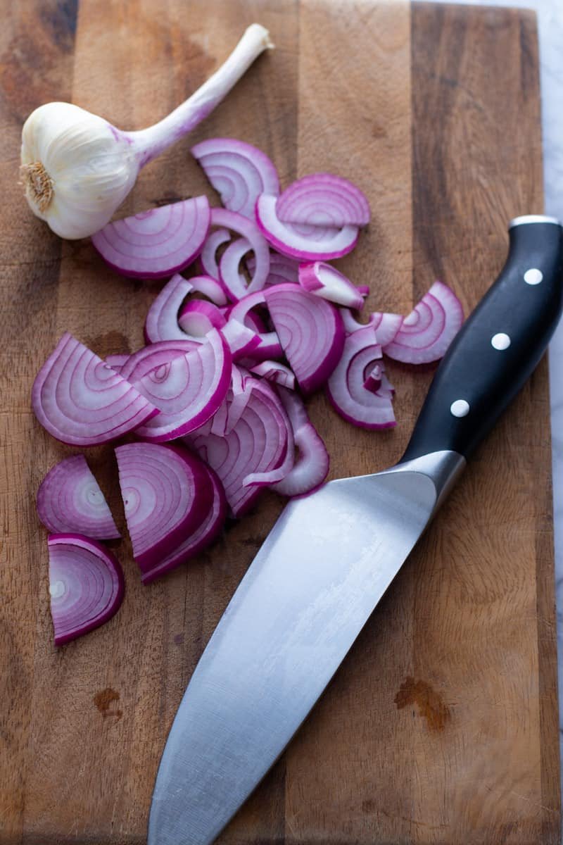 Chopped red onion, garlic and a chef's knife on a chopping board