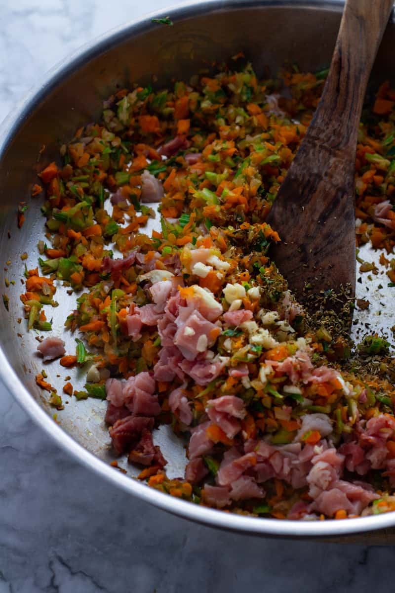 Red onions, carrots and celery in a frying pan with prosciutto 