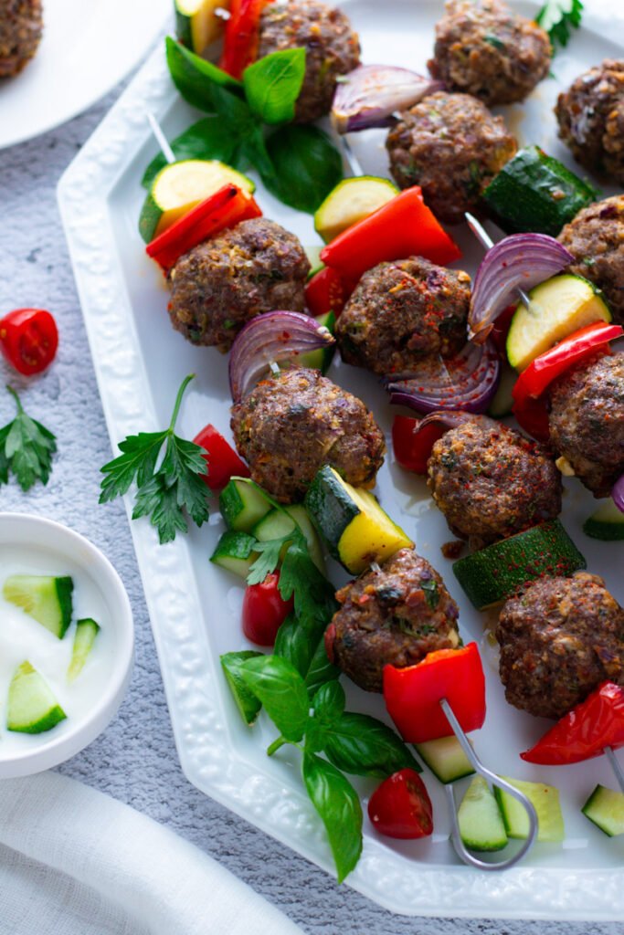 Mediterranean meatball skewers with mixed vegetables on a white plate