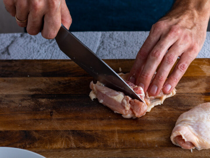 Using kitchen knife to cut raw chicken leg away from flesh