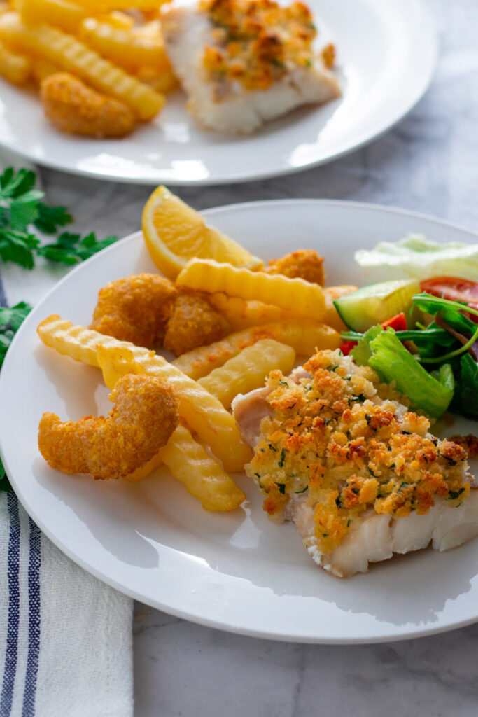 A plate of baked breaded cod with oven fries and salad.
