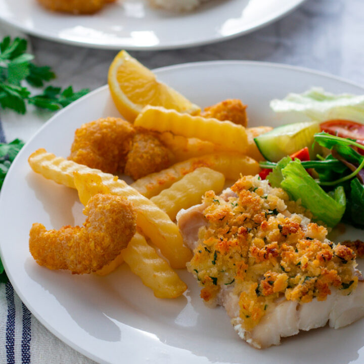 A plate of baked breaded cod with oven fries and salad.