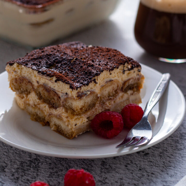 A slice of beeramisu with raspberries and a beer in the background.