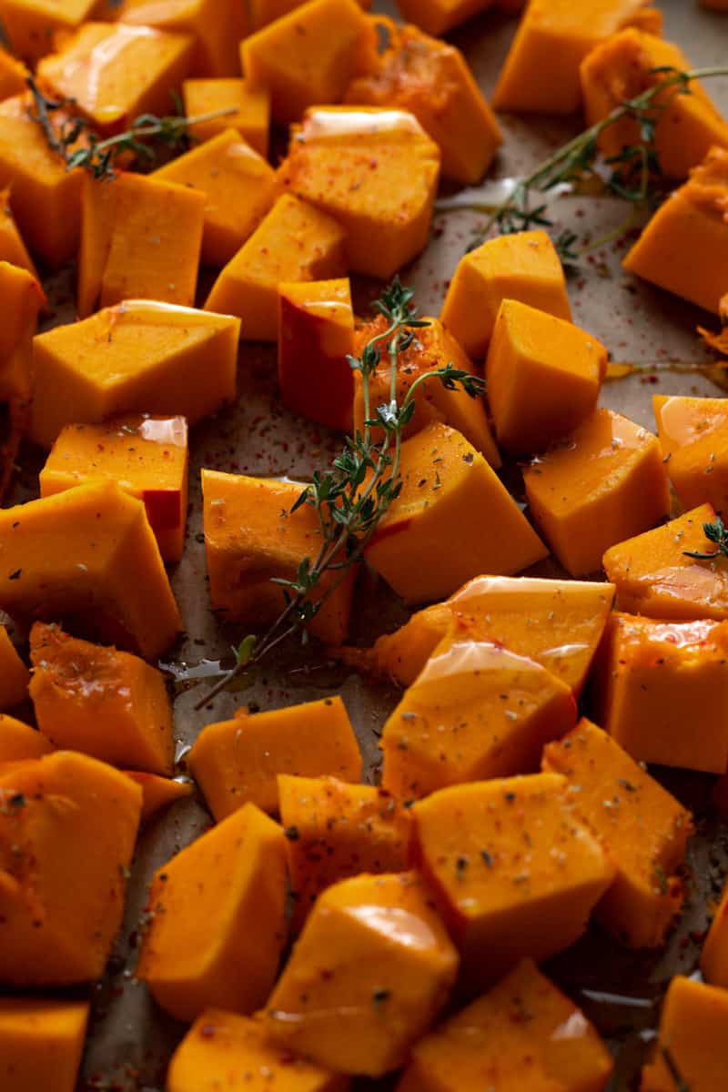 Chopped pumpkin with thyme on a baking tray.