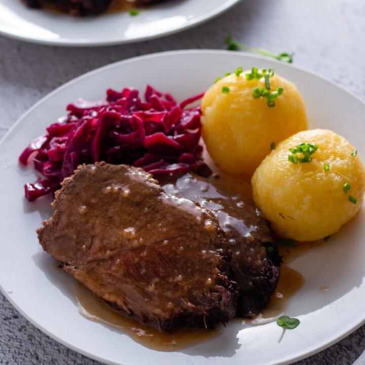 German Sauerbraten beef roast on a plate with red cabbage and potato dumplings.