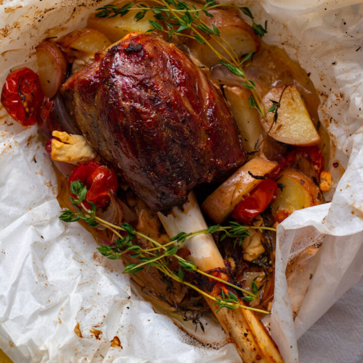 Greek Lamb Shank in parchment paper with potatoes, olives, tomatoes and onions.