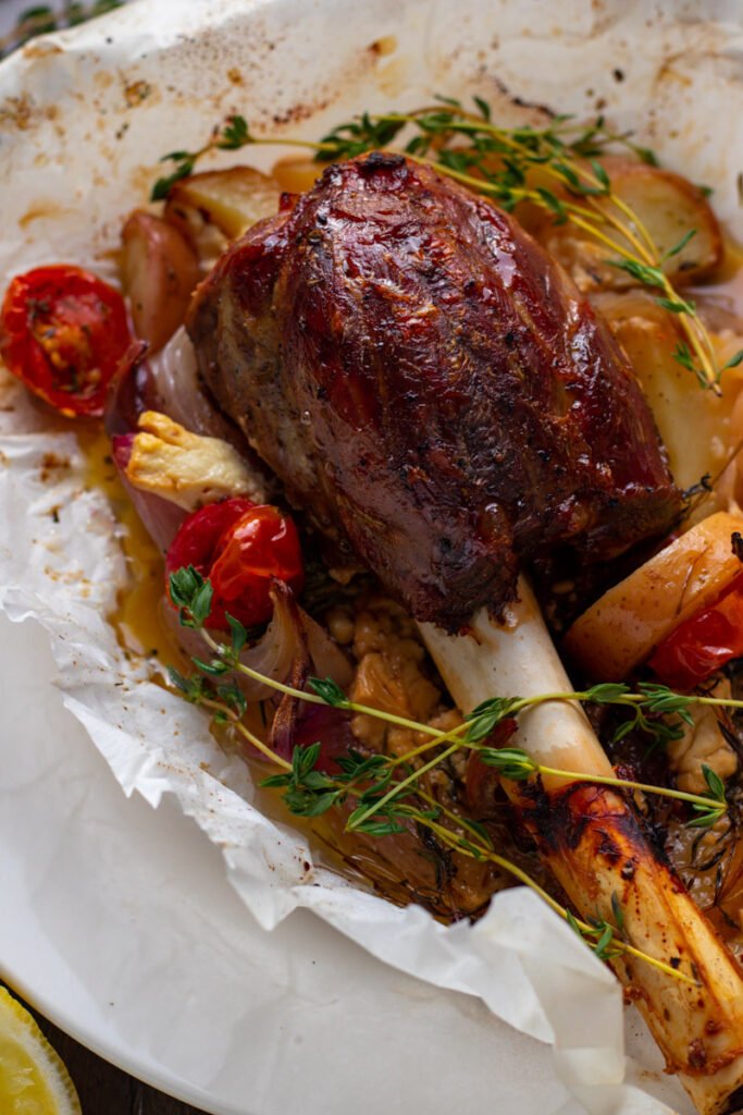 Greek Lamb Shank in parchment paper with potatoes, olives, tomatoes and onions.