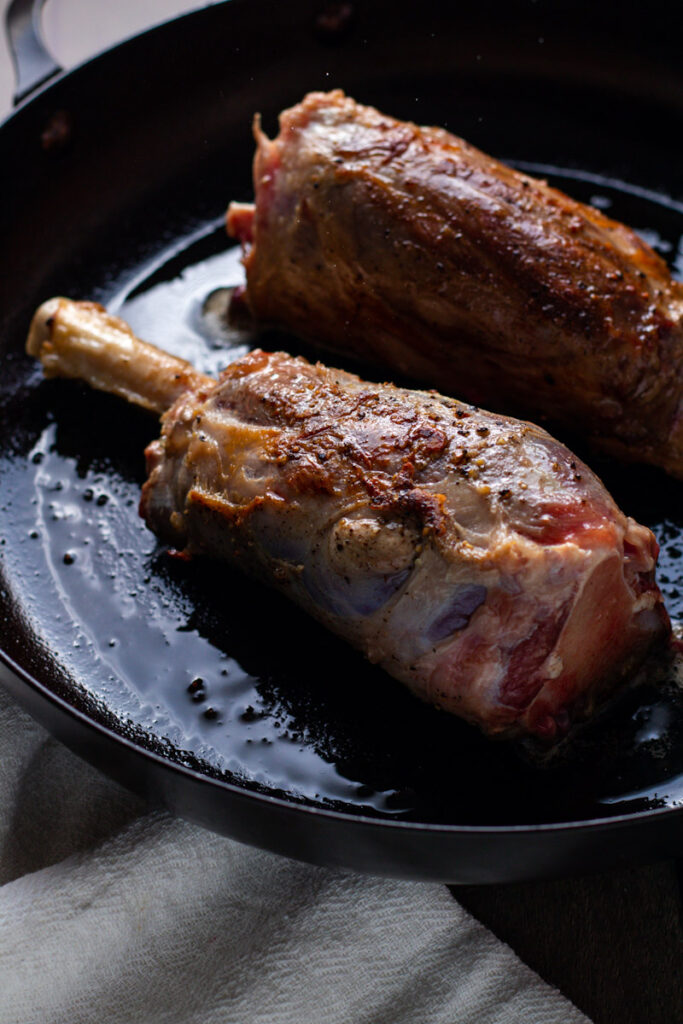 Lamb shanks browning in a skillet.