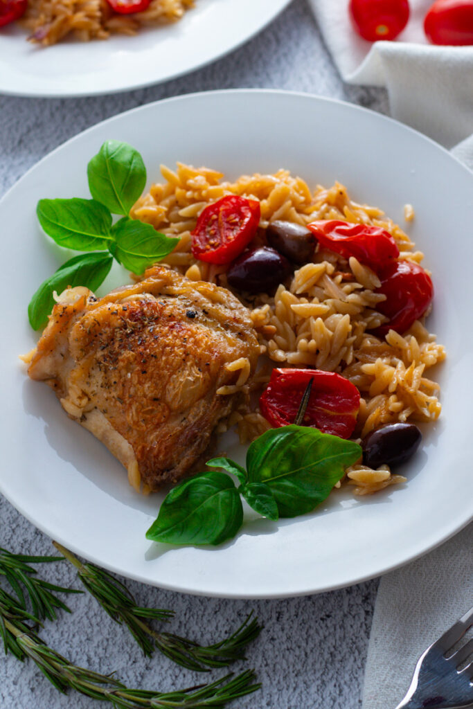 One pan chicken and orzo on a plate with fresh herbs.