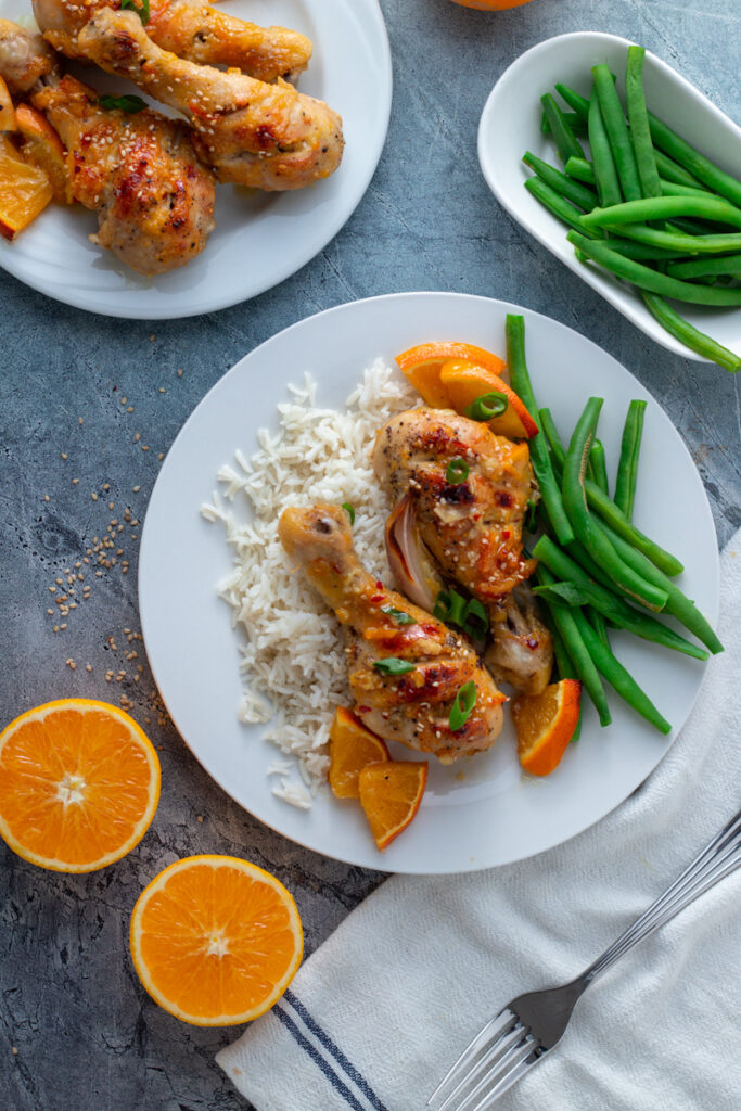 Sticky Orange Chicken drumsticks on a plate with white rice and green beans.