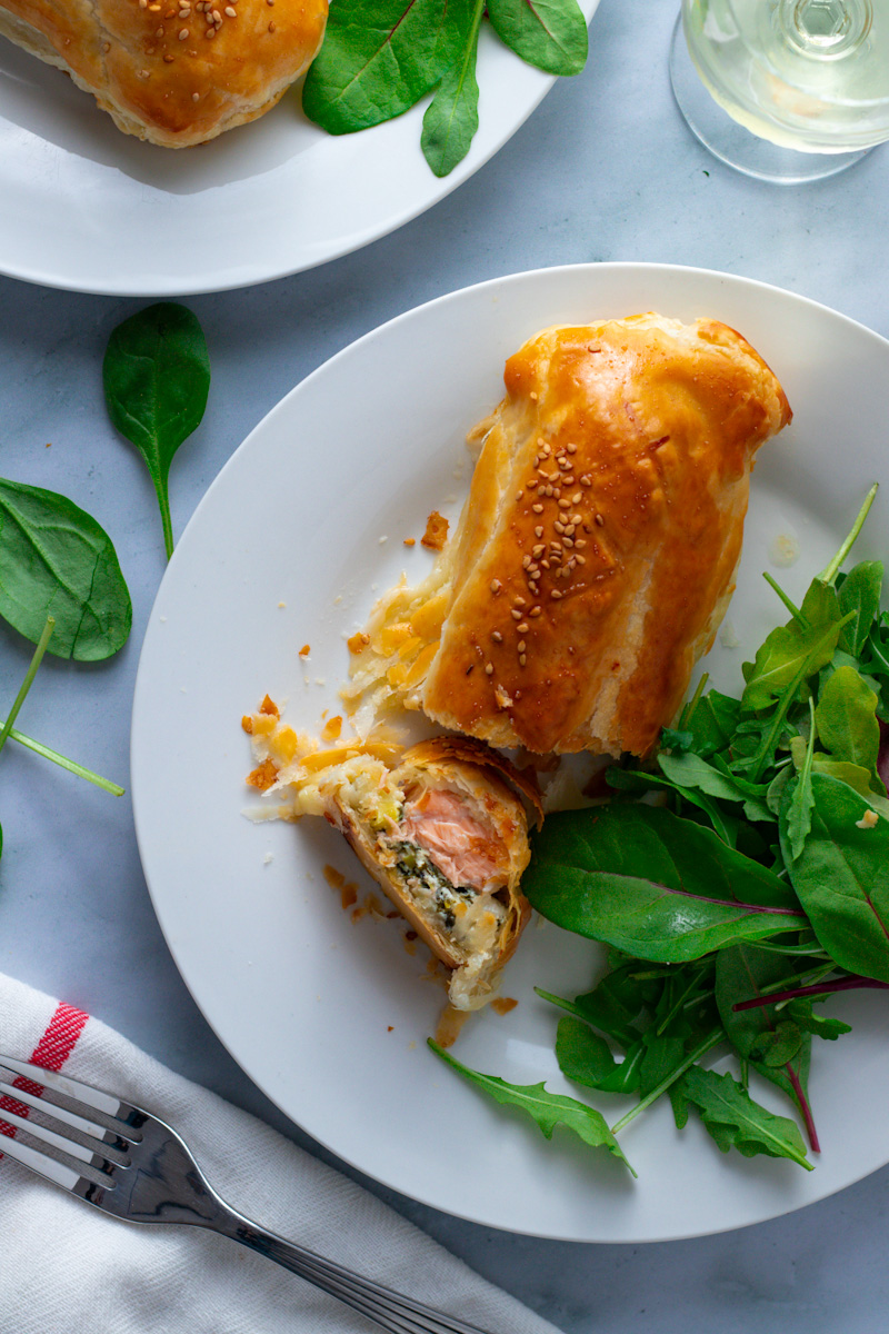 Salmon en Croûte or Salmon Wellington on a plate with fresh green salad and a glass of wine.