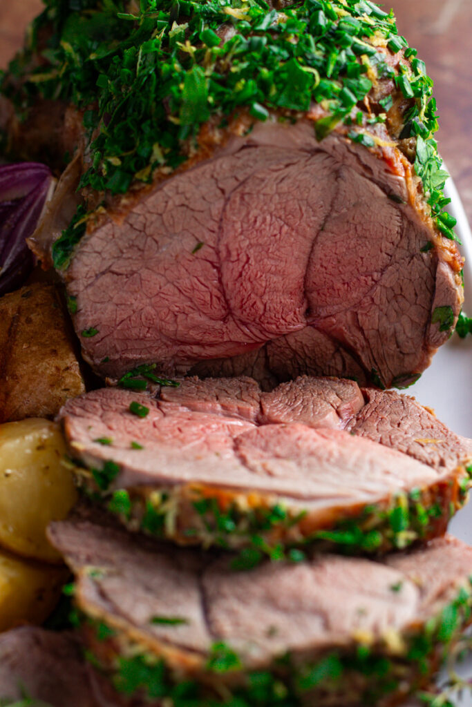 Roast Lamb with fresh herb crust, sliced, showing perfect rosy pink, medium-rare interior.