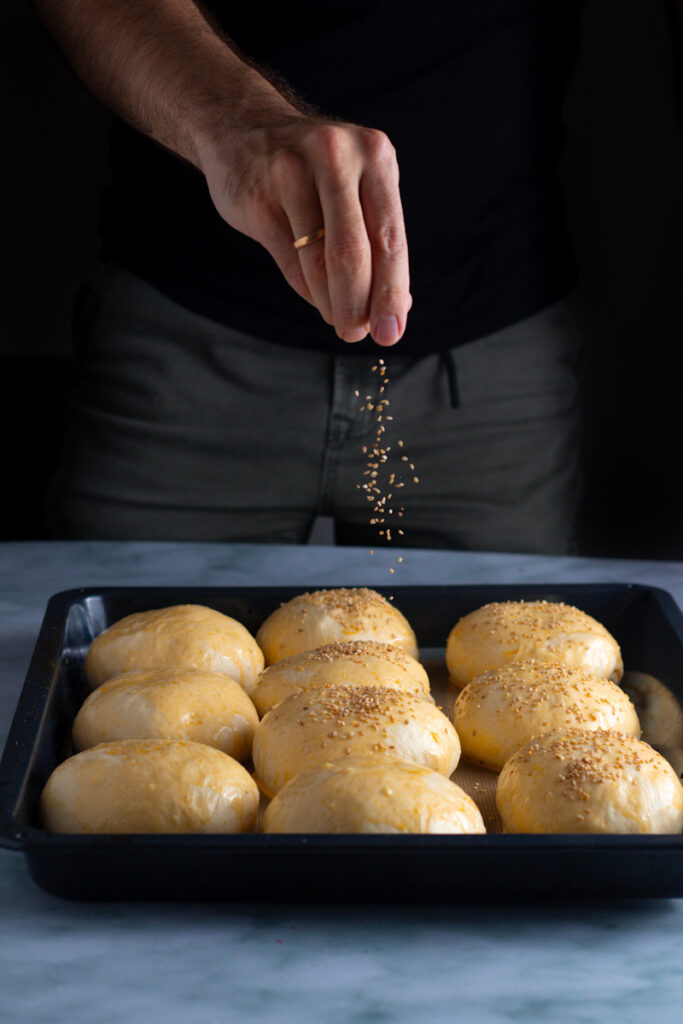 Jay Wadams sprinkling sesame seeds onto unbaked potato buns.