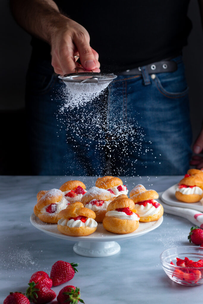 Jay Wadams shaking powdered sugar onto a cake stand of strawberry cream puffs.