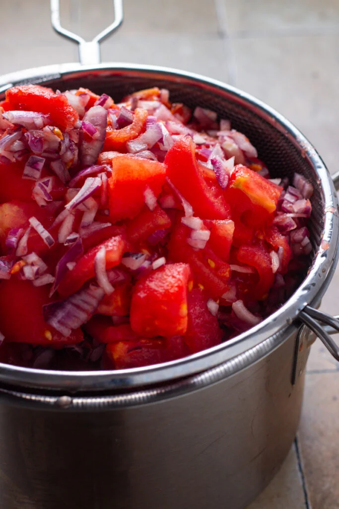 Salted tomatoes and onions in a sieve.