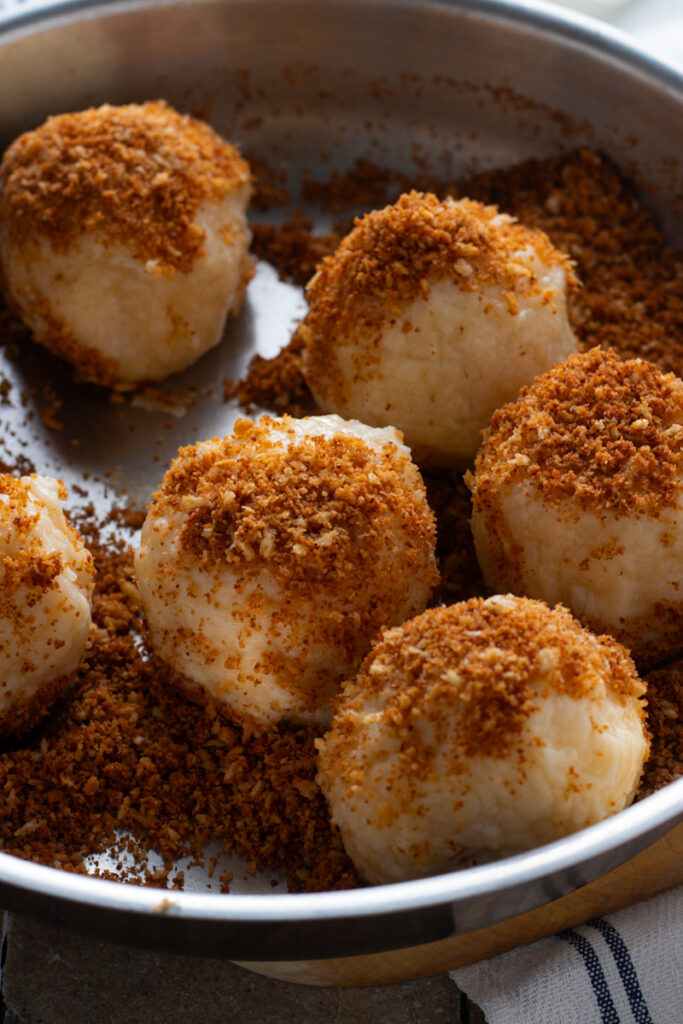 Apricot dumplings being rolled in breadcrumbs.