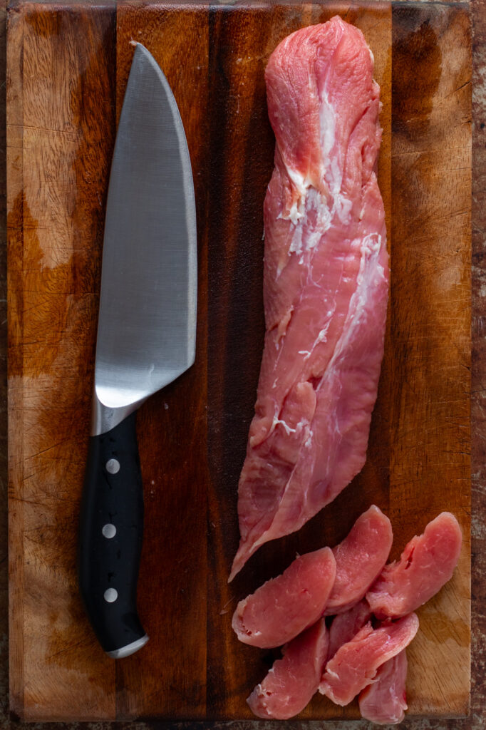 Pork tenderloiun and a knife on a cutting board.