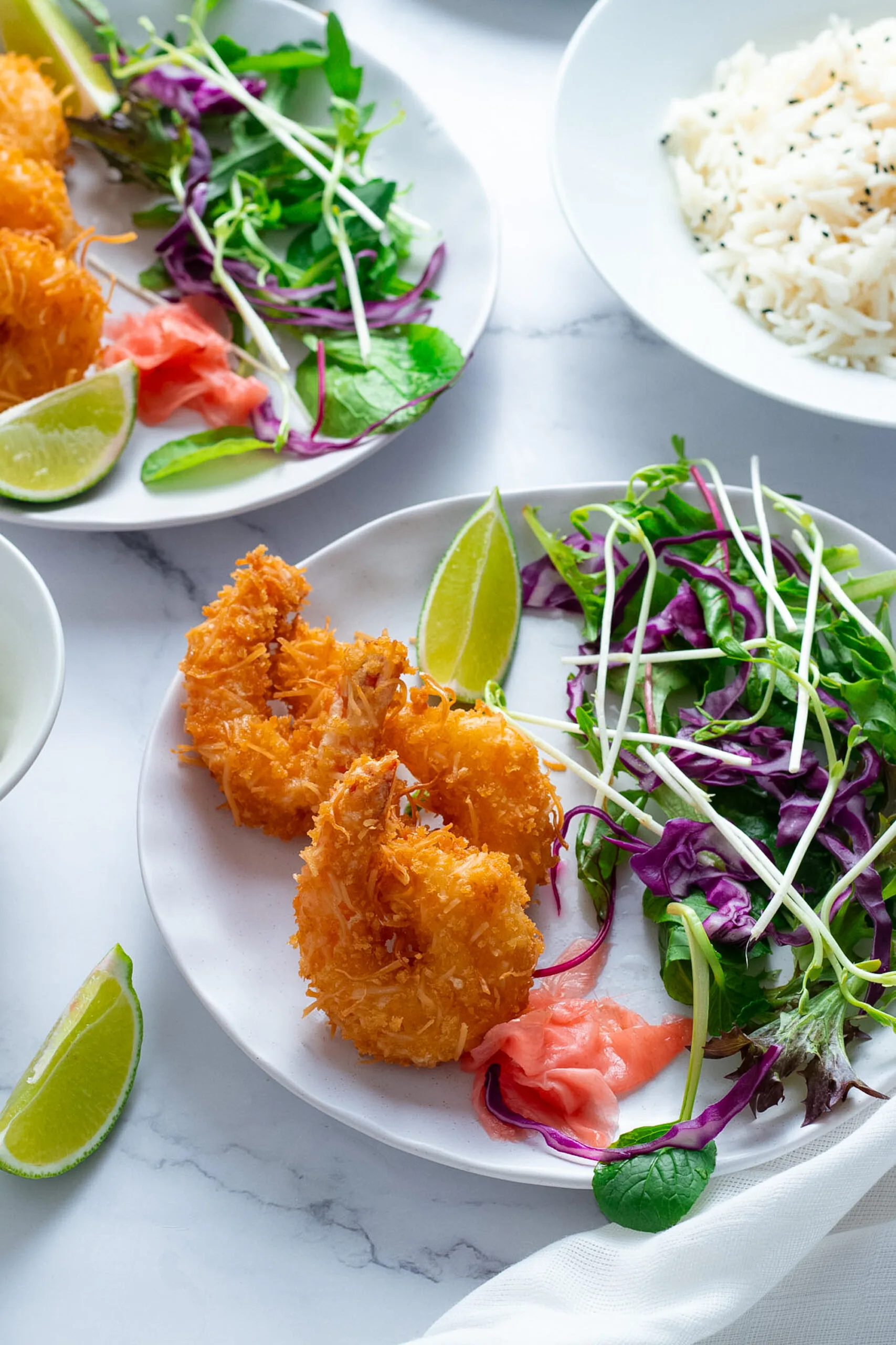 Panko Coconut Fried Shrimp on a plate with salad and lime wedges.