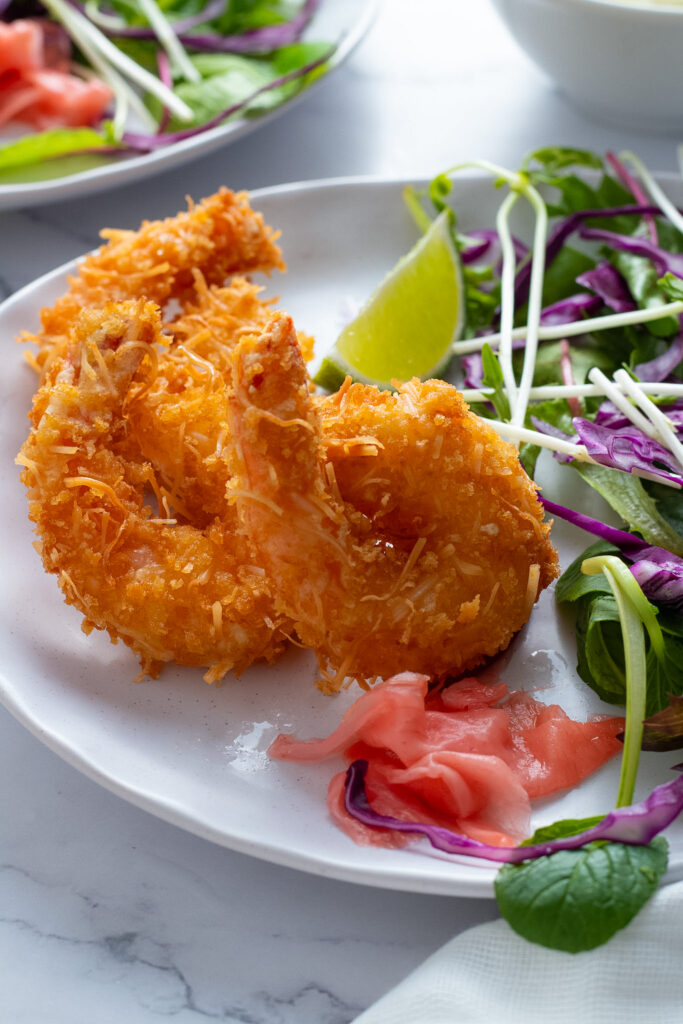 Panko Coconut Fried Shrimp on a plate with salad and lime wedges.