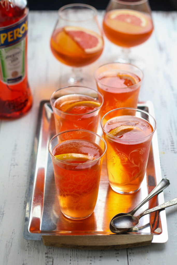 Aperol Spritz jellies in glasses with orange slice garnish with a bottle of aperol in the background.