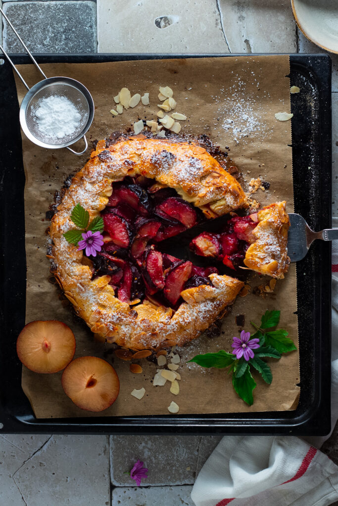 Plum Galette seen from above with sugar, flowers and fresh plums.