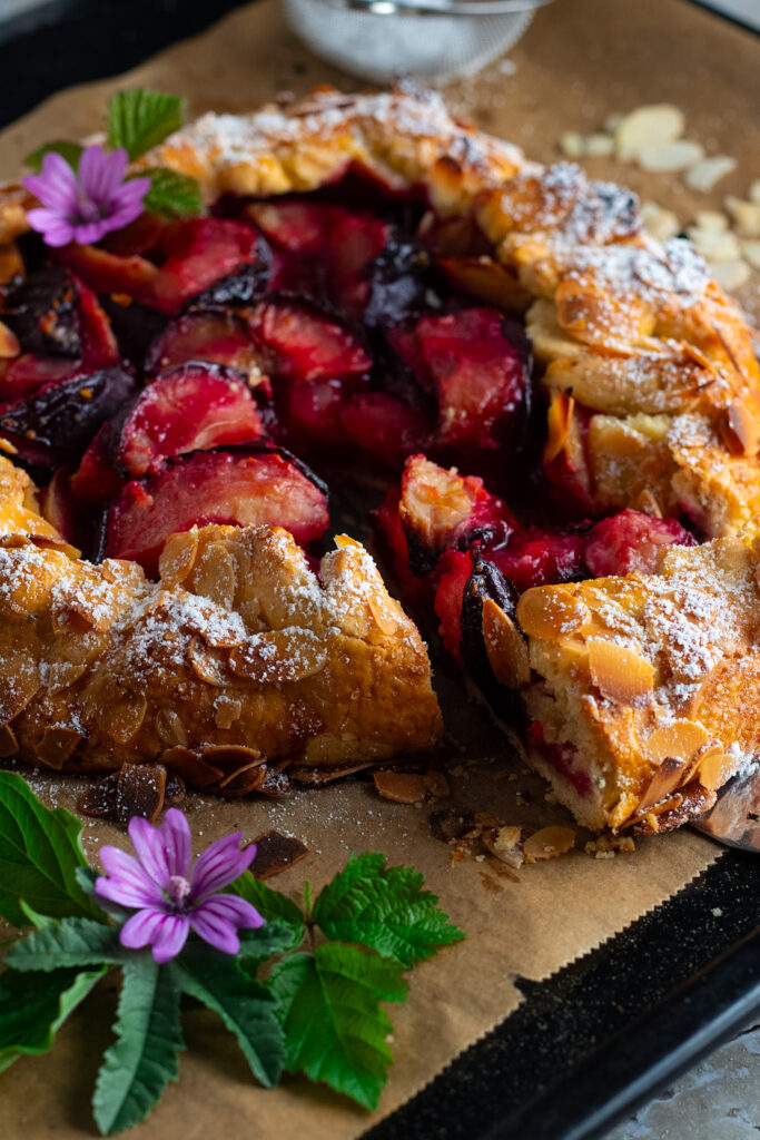 Rustic free form plum tart with a slice out on a tray.