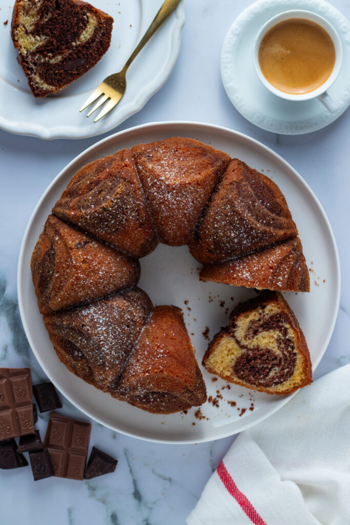 Marble cake (Marmorkuchen) on a plate with coffee and chocolate. Slices are cut, revealing the marble pattern.
