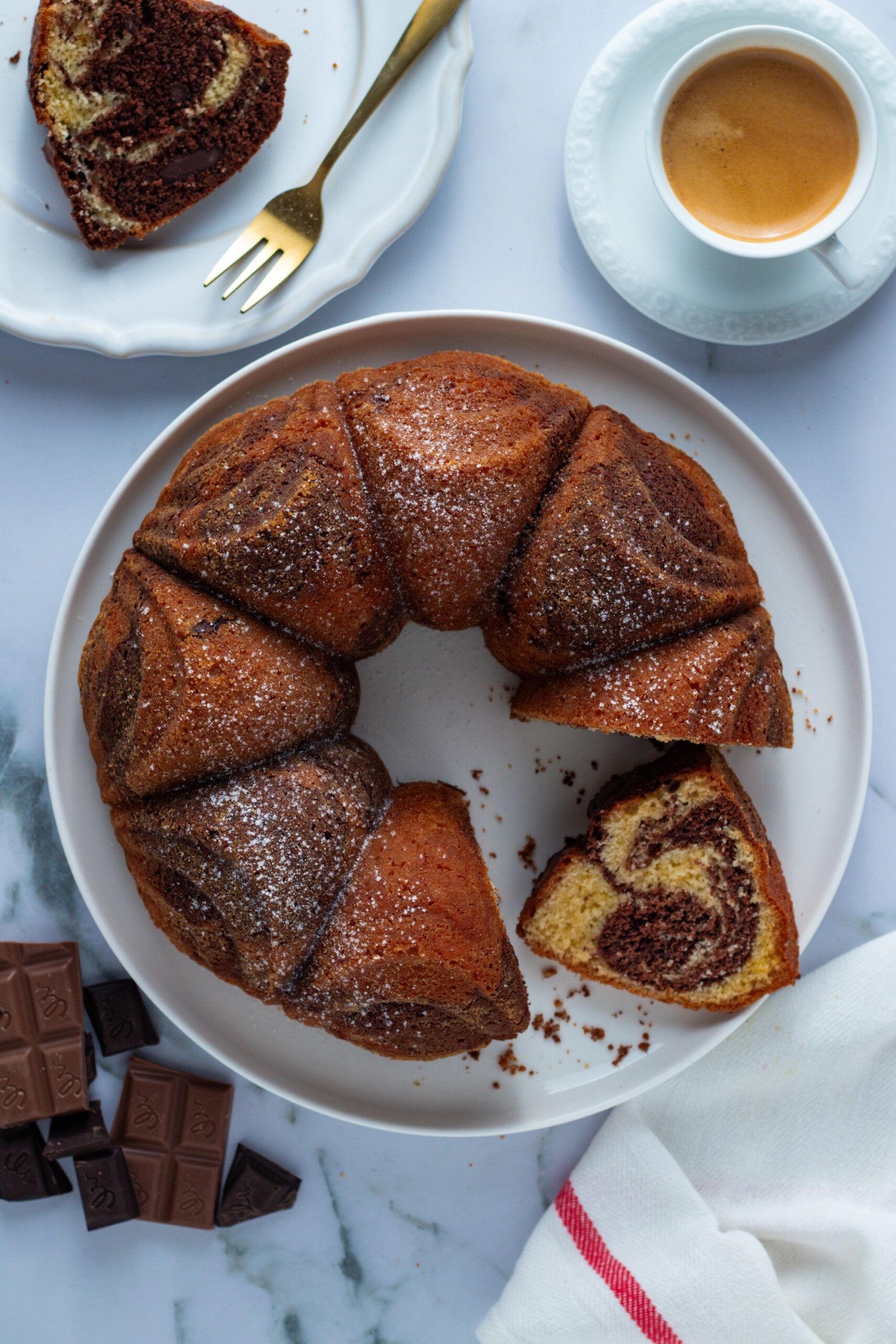 Marble cake (Marmorkuchen) on a plate with coffee and chocolate. Slices are cut, revealing the marble pattern.