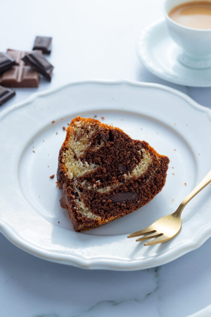 Slice of German Marble Cake (Marmorkuchen) on a white plate with a gold fork and cup of coffee.