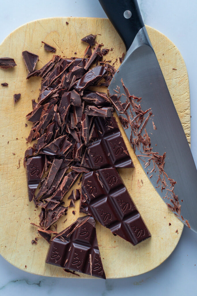 Chopped dark chocolate on a cutting board with a knife, preparing for Marmorkuchen (German Marble Cake).